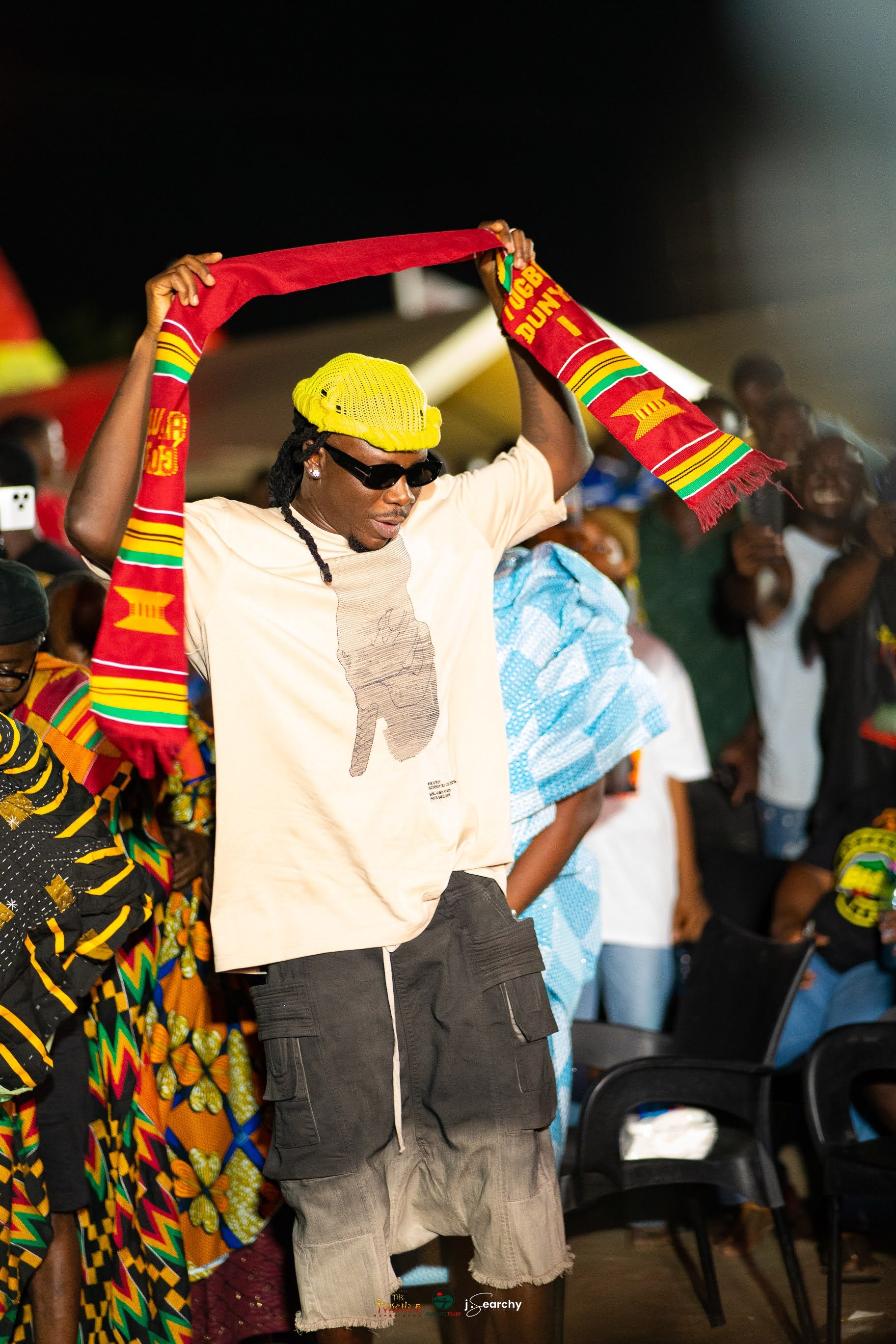 Stonebwoy raises his arms in a white smock and kente sash at the Torcher Experience celebration